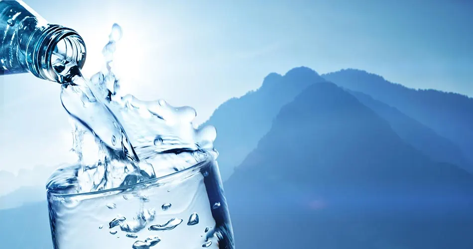 Wasser fließt in ein Glas, im Hintergrund Berge