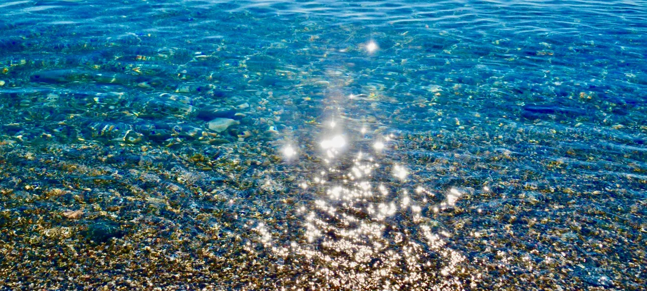 Sonnenlicht glitzert auf klarem Wasser über Kieselsteinen